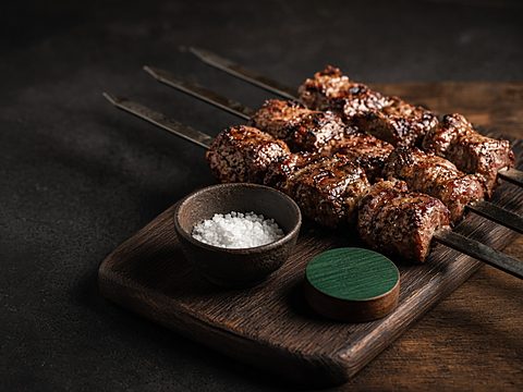 Grilled beef on skewers on a carving board with coarse salt and a green table token