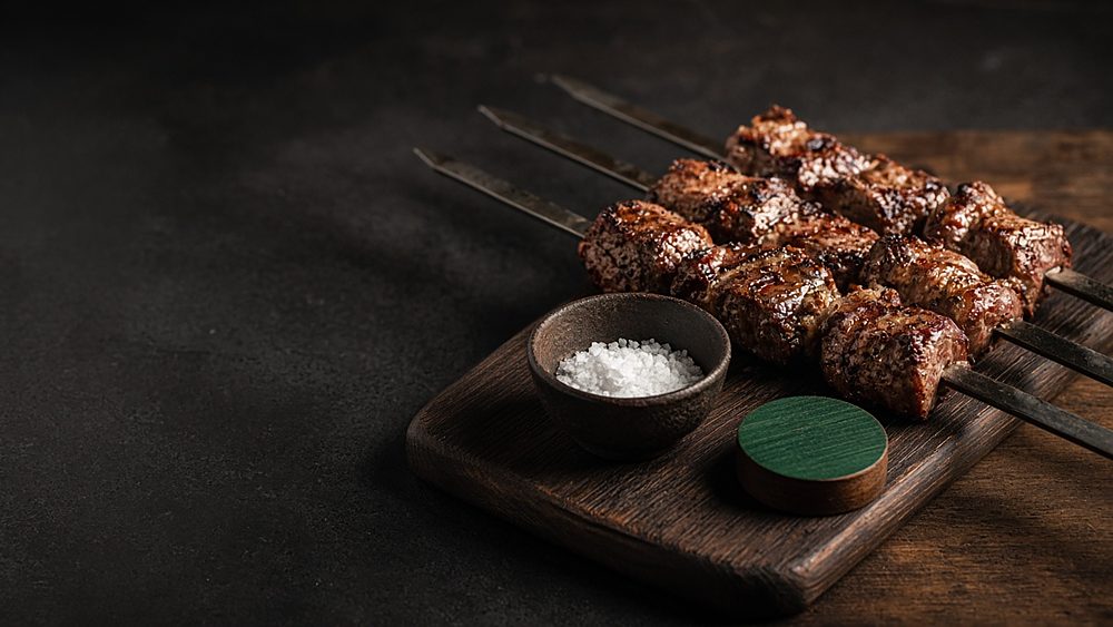 Grilled beef on skewers on a carving board with coarse salt and a green table token