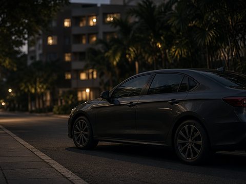 A dark sedan parked at a quiet, lit curb at dusk with apartment buildings behind