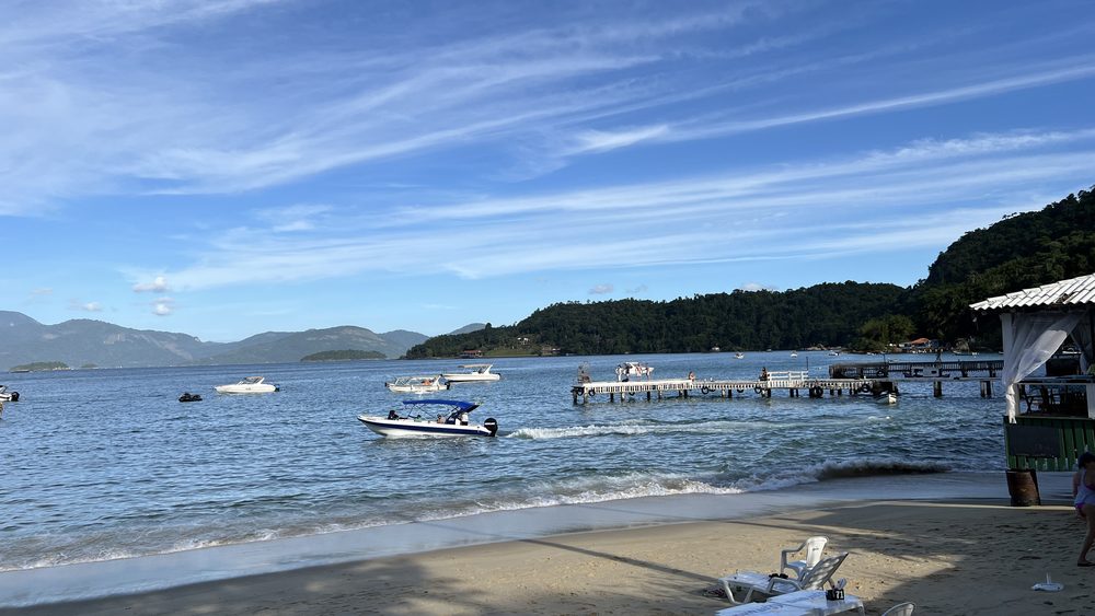 A bay with moored boats, a pier, and tables set out on the sand