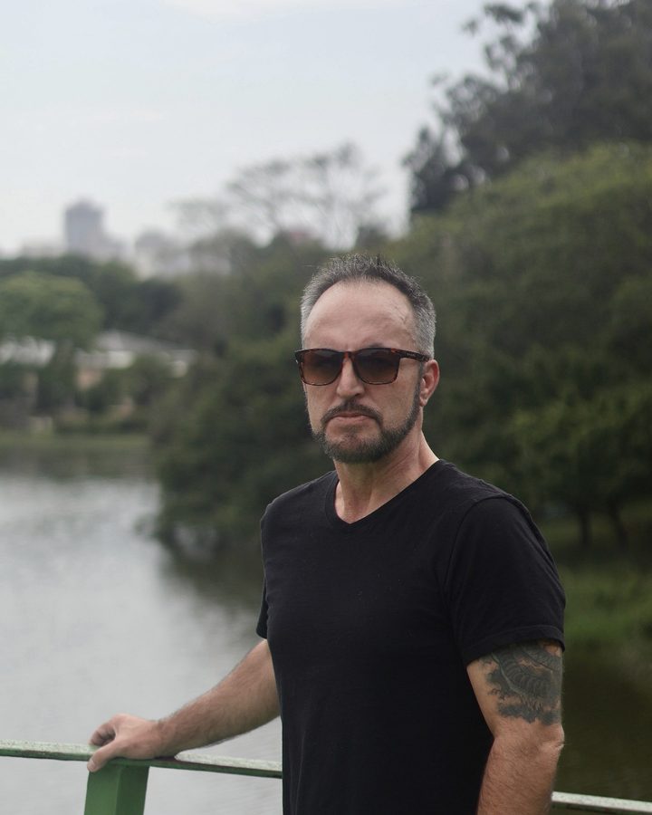 Vaughn Bullard in a black T-shirt and sunglasses, standing at a green railing by the water
