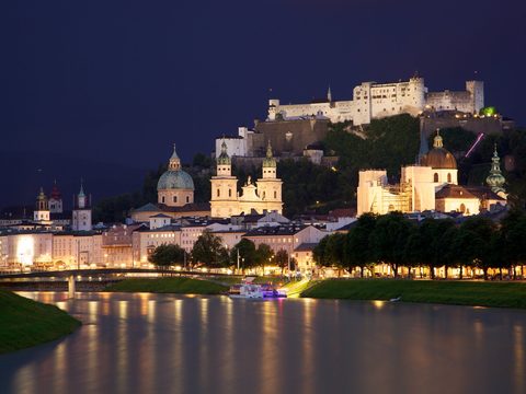 Salzburg old town and fortress lit at night across the Salzach river