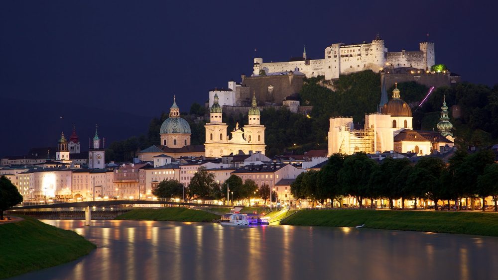 Salzburg old town and fortress lit at night across the Salzach river