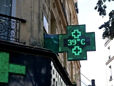 Green illuminated pharmacy cross sign on a Paris street