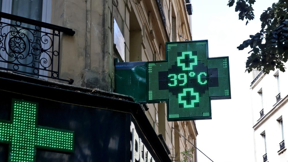 Green illuminated pharmacy cross sign on a Paris street