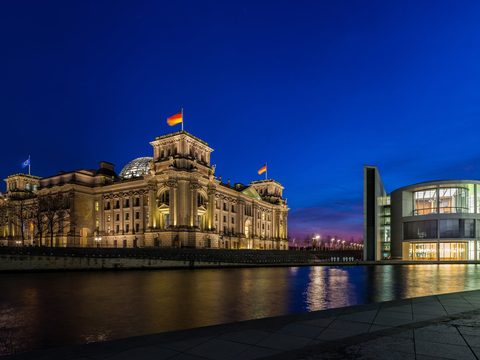 The Reichstag and Berlin's government quarter lit up at dusk beside the Spree