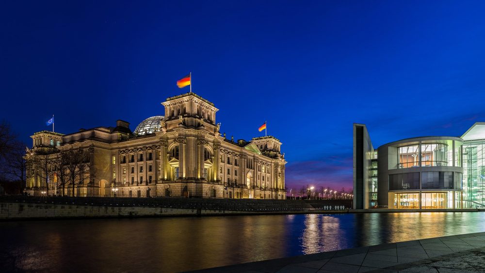The Reichstag and Berlin's government quarter lit up at dusk beside the Spree