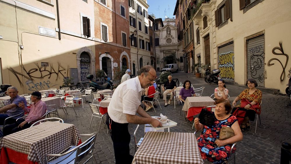 Waiter serving diners at outdoor tables of a street cafe in Rome