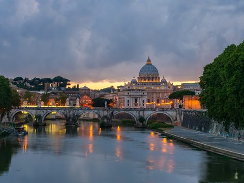 Ponte Sant'Angelo over the Tiber in Rome at dusk, with the dome of St. Peter's Basilica behind
