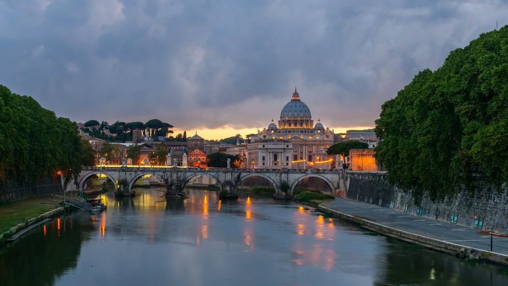 Ponte Sant'Angelo over the Tiber in Rome at dusk, with the dome of St. Peter's Basilica behind