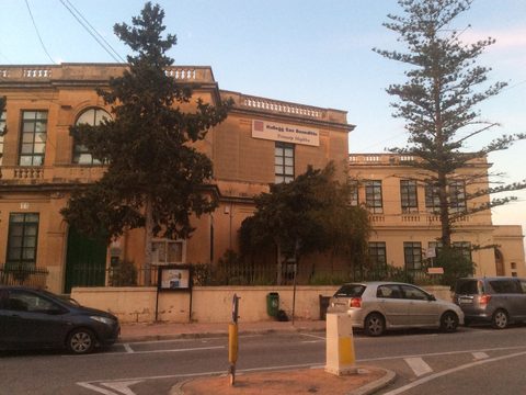 Stone primary school building in Mqabba, Malta, with palm and pine trees