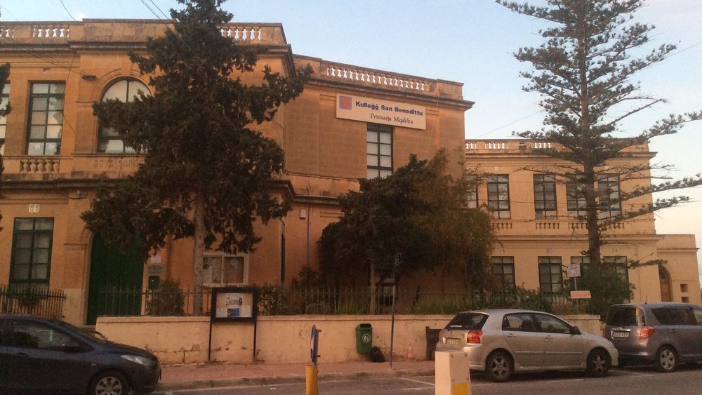 Stone primary school building in Mqabba, Malta, with palm and pine trees