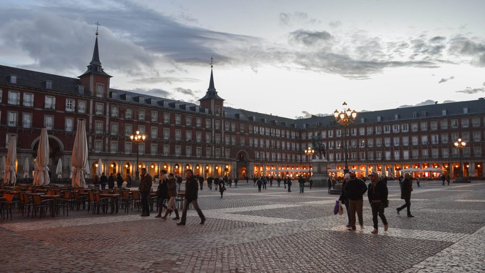 Plaza Mayor in central Madrid with its red arcaded buildings and pedestrians crossing the square