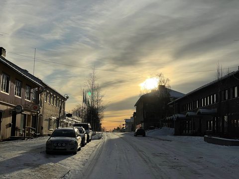 Cars parked on a snowy street in Overtornea, northern Sweden, at sunset