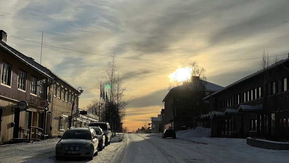 Cars parked on a snowy street in Overtornea, northern Sweden, at sunset