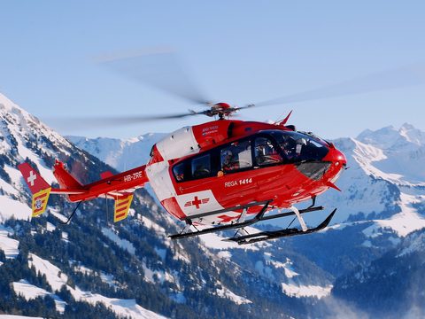 Rega air rescue helicopter flying in front of snowy Swiss Alps