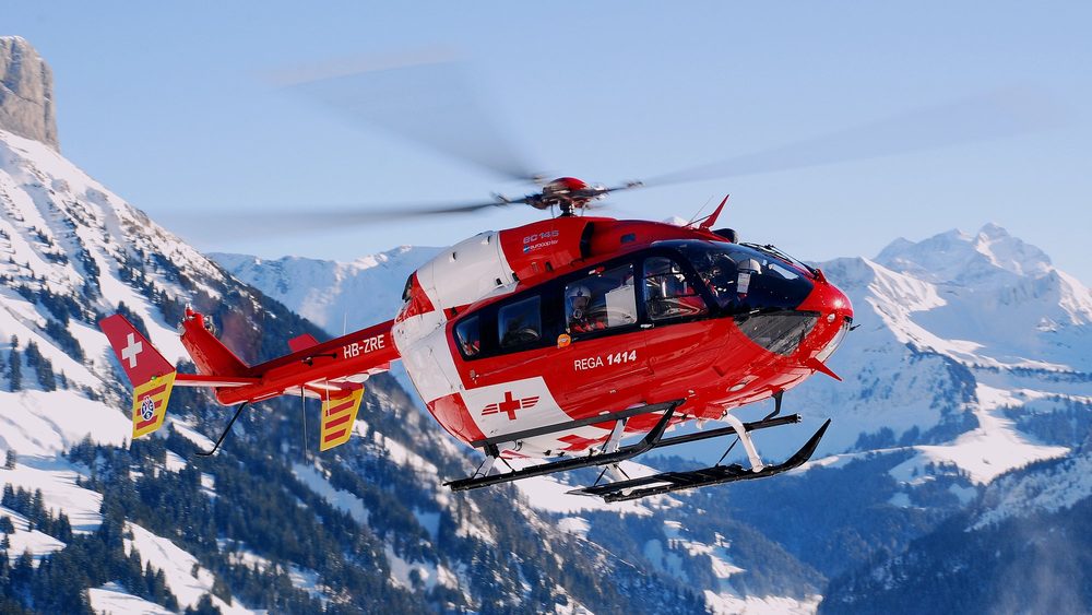 Rega air rescue helicopter flying in front of snowy Swiss Alps