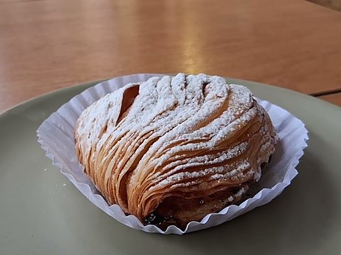 A sfogliatella, the layered shell-shaped pastry, dusted with powdered sugar in a paper case on a green plate