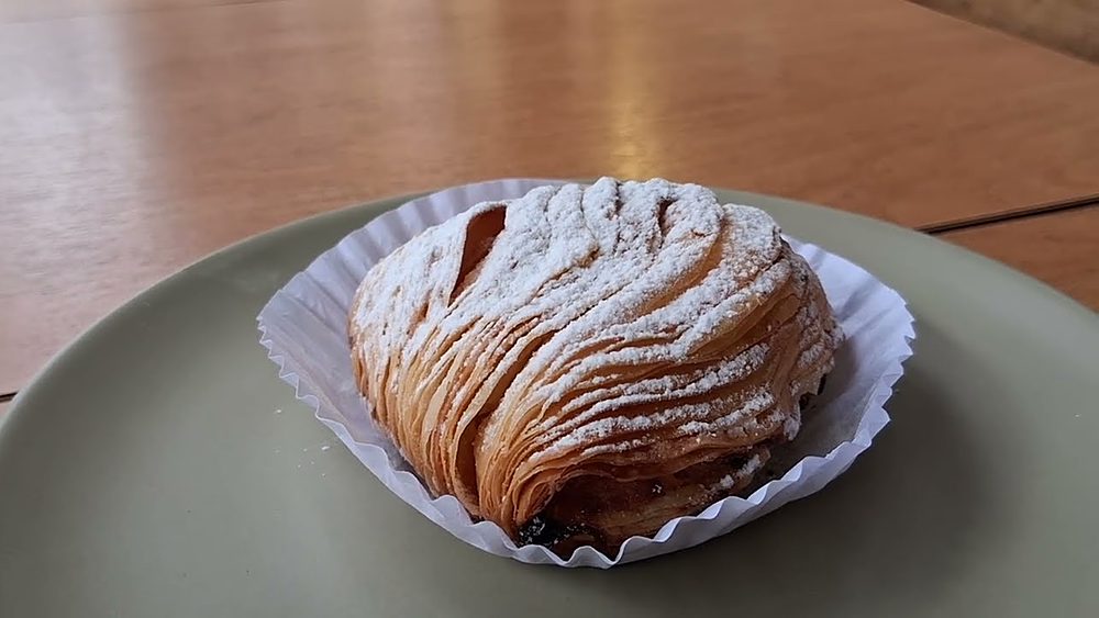 A sfogliatella, the layered shell-shaped pastry, dusted with powdered sugar in a paper case on a green plate